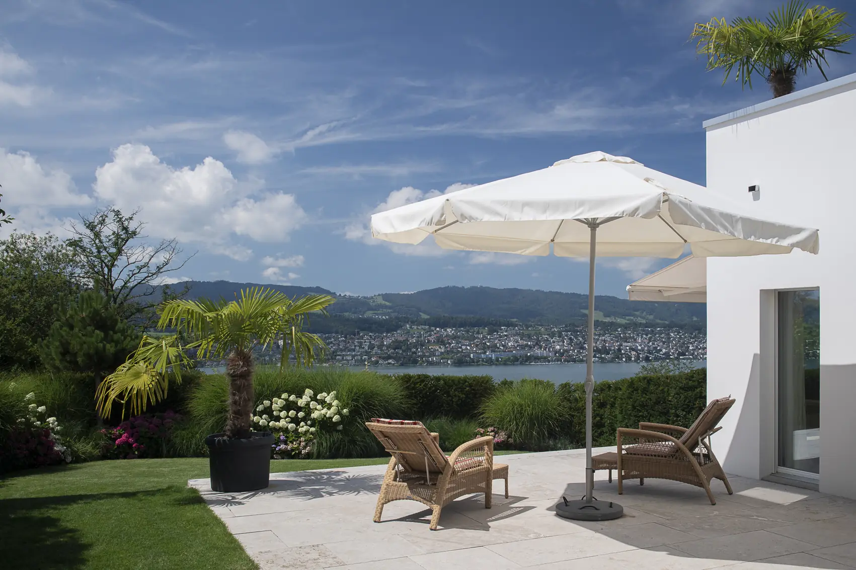 Terrasse mit Sonnenschirm und Liegestühlen mit Blick über den See